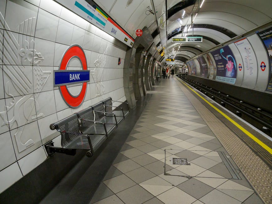 An empty platform at Colindale Tube station NW9 featuring white tiled walls with embossed decorative patterns, including a large London Underground roundel sign in red and blue reading 'BANK,' mounted